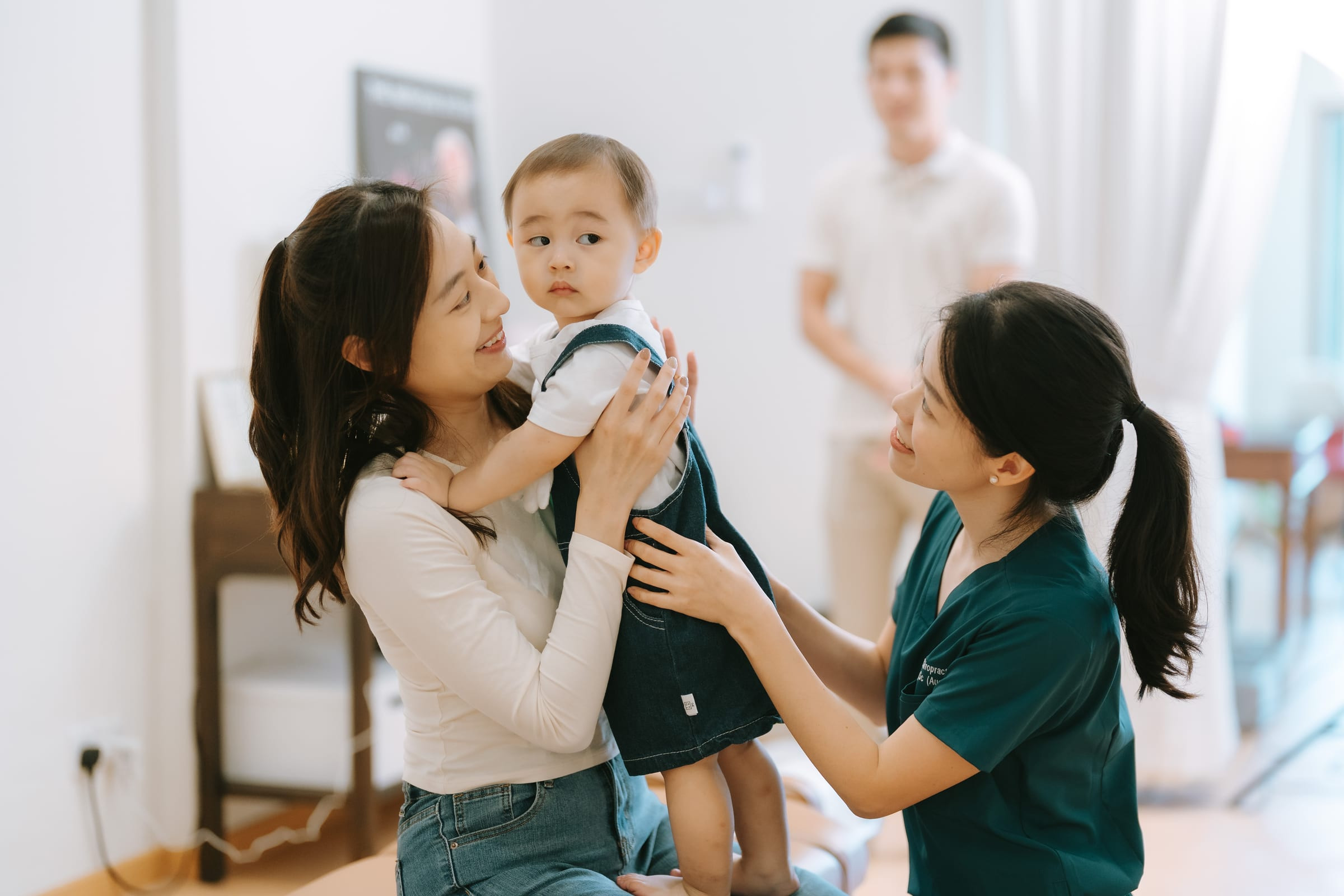 A pregnant mother holding her baby while the chiropractor assesses spinal function and development
